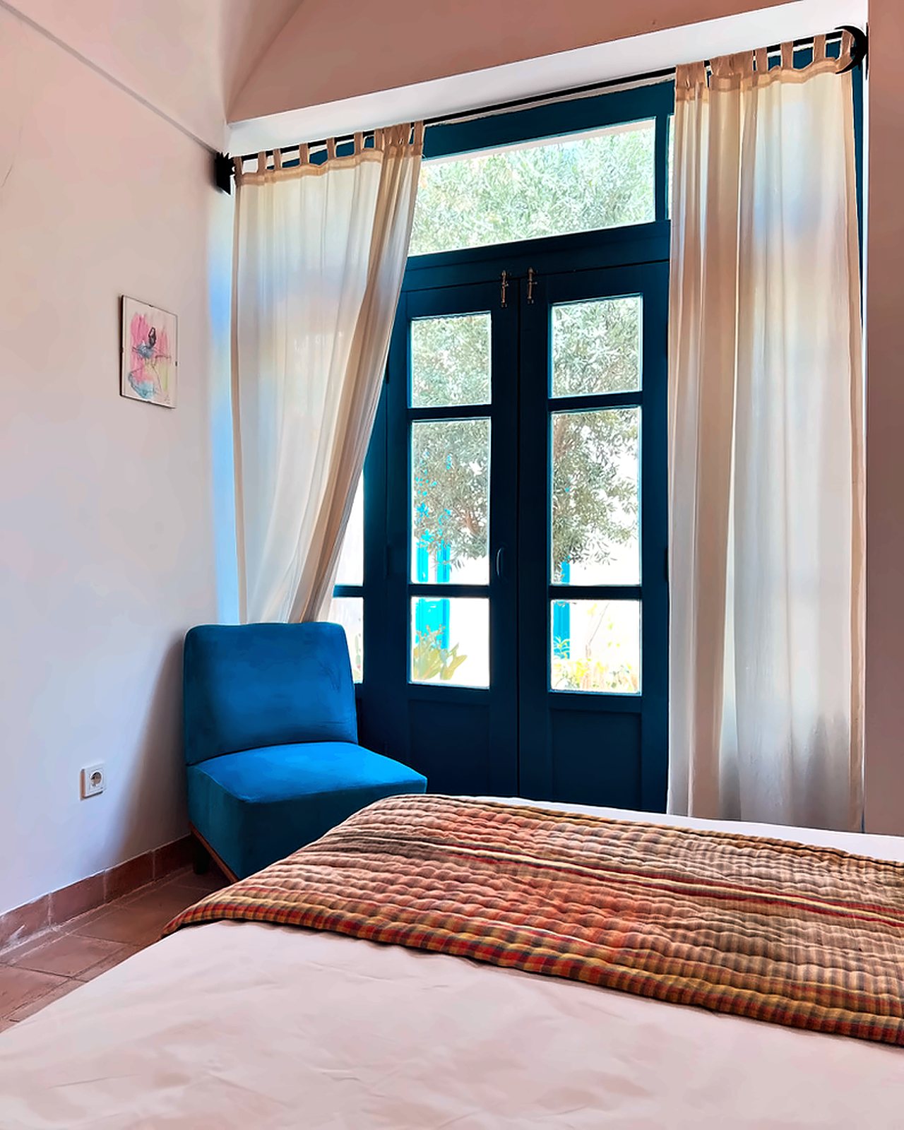 Chelcheragh: the bed with a striped Yazdi throw, a blue armchair and tall turquoise doors open onto the olive tree in the courtyard
