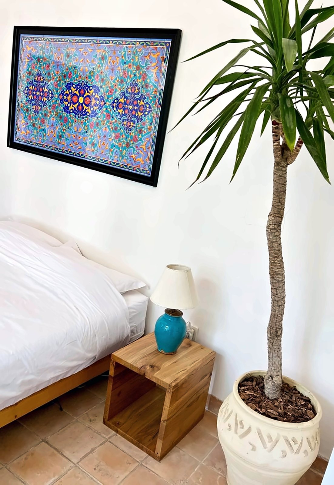 Chelcheragh: a white bed, a turquoise lamp and a tall yucca under a high white wall
